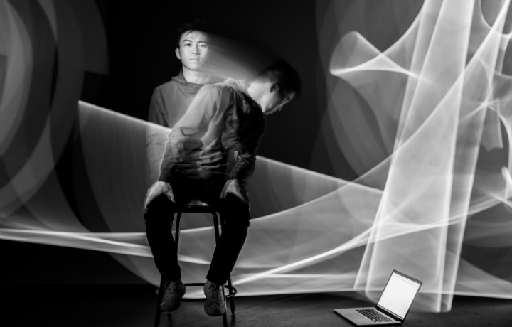 abstract image of person on a stool looking at a computer on the ground with light swirls behind them